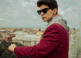 Elegant man in red jacket with sunglasses gazing over Ciudad de México skyline, exuding modern fashion.